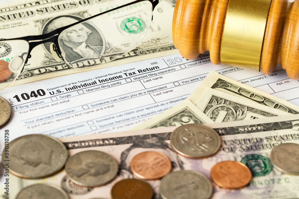 Closeup image of american 1040 Individual Income Tax return form with american dollar money, coins, glasses and judge gavel. Closeup image of american 1040 Individual Income Tax return form with american dollar money, coins, glasses and judge gavel.