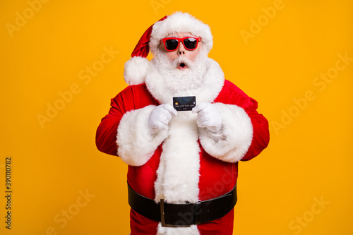 Portrait of his he nice attractive amazed stunned wondered Santa holding in hand bank card budget safe shopping investment isolated bright vivid shine vibrant yellow color background