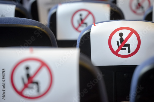 Shallow depth of field with social distance warning signs on seats during a show, concert or play in a theater or cinema, conference hall. Empty rows of places marked with a warning 'don't sit' sign.