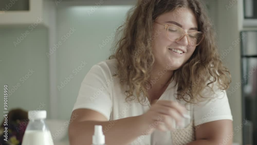 Portrait of Caucasian woman disinfecting hands with sanitizer before taking apple. Young chubby lady in eyeglasses sanitizing palms before eating. Covid-19 pandemic lifestyle. Portrait of Caucasian woman disinfecting hands with sanitizer before taking apple. Young chubby lady in eyeglasses sanitizing palms before eating. Covid-19 pandemic lifestyle.
