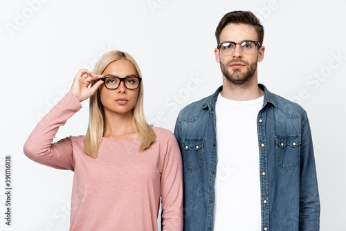 Young woman touching eyeglasses near boyfriend isolated on grey