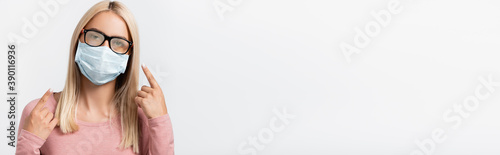 Blonde woman in medical mask pointing at misted eyeglasses isolated on grey  banner