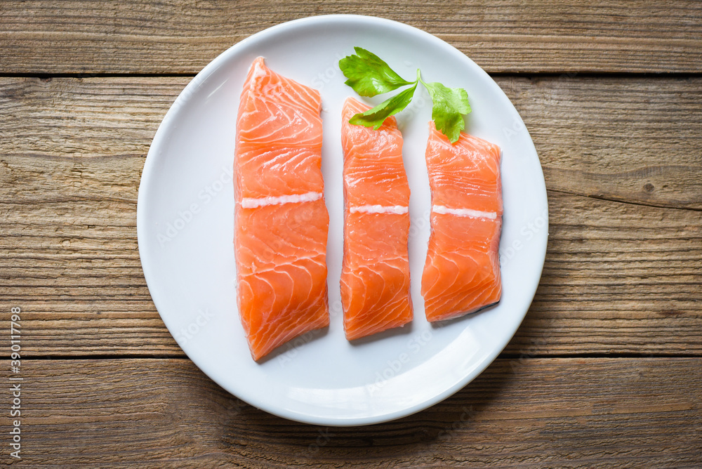 Raw salmon filet with herbs and spices on white plate and wooden background Raw salmon filet with herbs and spices on white plate and wooden background
