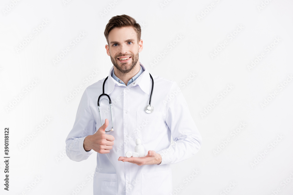 Front view of smiling ophthalmologist with thumb up, holding lenses container and plastic bottle isolated on white Front view of smiling ophthalmologist with thumb up, holding lenses container and plastic bottle isolated on white