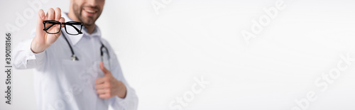 Cropped view of doctor with thumb up, showing eyeglasses with black frame isolated on white on blurred background, banner