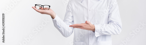 Cropped view of ophthalmologist holding and pointing with hand at eyeglasses on palm isolated on white, banner