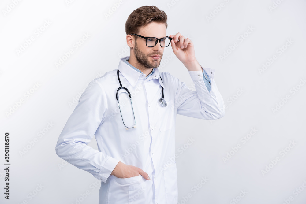 Confident doctor with hand in pocket holding eyeglasses frame, while looking away isolated on white Confident doctor with hand in pocket holding eyeglasses frame, while looking away isolated on white