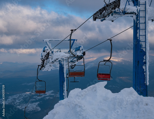 Alpine resort ski lift with seats going over the sunset mountain skiing  slopes in extremally windy weather photo