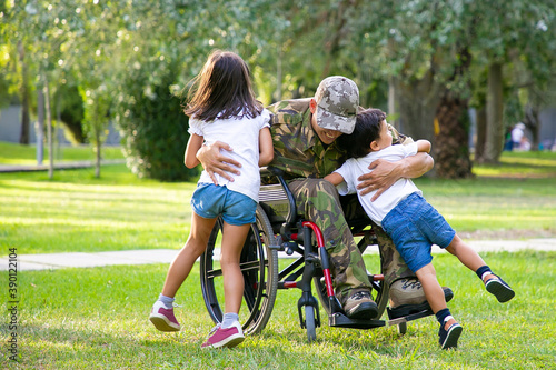 Happy disabled military man in wheelchair returning home and hugging kids. Veteran of war or family reunion concept