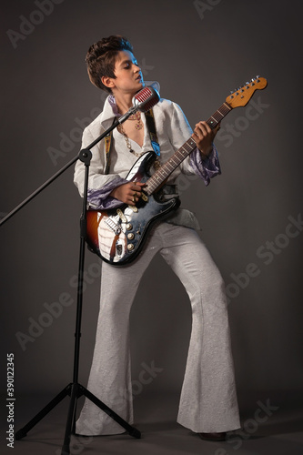 A teenage guy in the image of Elvis Presley with a guitar and a concert suit
