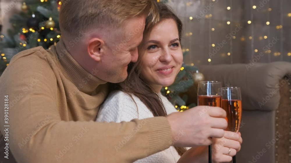 Young couple in love sitting and hugging near the Christmas tree and drinking a glass of champagne. Happy holiday in winter time. Young couple in love sitting and hugging near the Christmas tree and drinking a glass of champagne. Happy holiday in winter time.