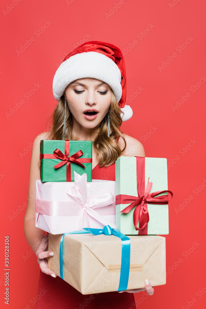 surprised woman in santa hat looking at gift boxes on red surprised woman in santa hat looking at gift boxes on red