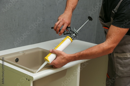 worker seals kitchen sink with sealant. hands of worker works with construction sealant gun in the kitchen.