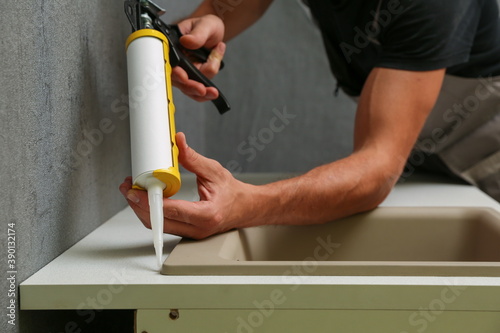 worker seals kitchen sink with sealant. hands of worker works with construction sealant gun in the kitchen. photo