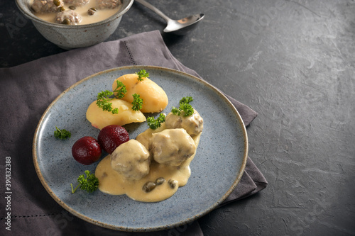 Boiled meatballs in Germany called Koenigsberger Klopse in a white bechamel sauce with capers, potatoes and beetroot on a blue plate, dark gray napkin and slate background with copy space photo