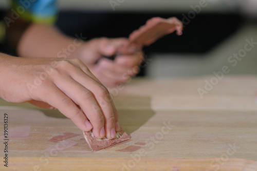 Young carpenter in work clothes and face mask using wood filler in finishing work for console table
