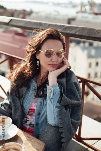 A beautiful middle-aged woman is sitting in a rooftop cafe with a Cup of coffee.