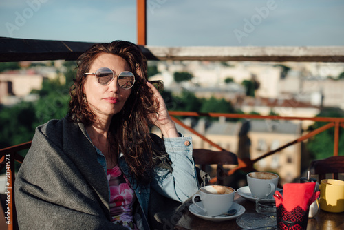 A beautiful middle-aged woman is sitting in a rooftop cafe with a Cup of coffee.