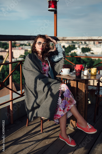 A beautiful middle-aged woman is sitting in a rooftop cafe with a Cup of coffee.