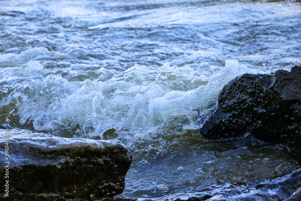 waves run onto the shore and crash against the rocks, creating many splashes and splashes near the shore. river surf in stormy weather near a stone pebble coast with foamy splashing waves. waves run onto the shore and crash against the rocks, creating many splashes and splashes near the shore. river surf in stormy weather near a stone pebble coast with foamy splashing waves.