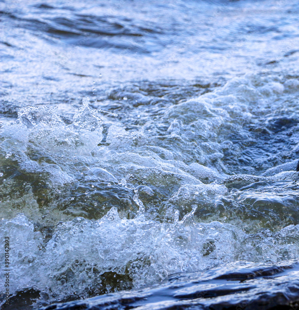 Obraz premium waves run onto the shore and crash against the rocks, creating many splashes and splashes near the shore. river surf in stormy weather near a stone pebble coast with foamy splashing waves.