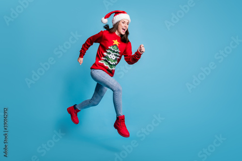 Full body size profile photo of cute lovely lady jump sprinting air hands fists open mouth wear santa x-mas headwear red ornamented pullover jeans boots isolated blue color background