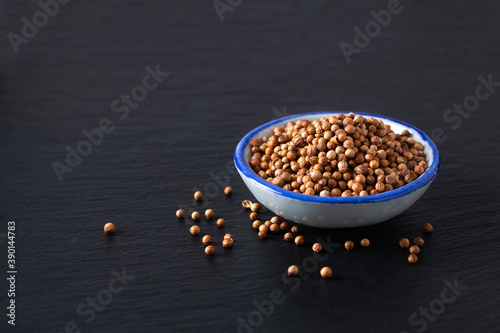 Food ingredient concept organic coriander seed in ceramic bowl on black slate stone board with copy space