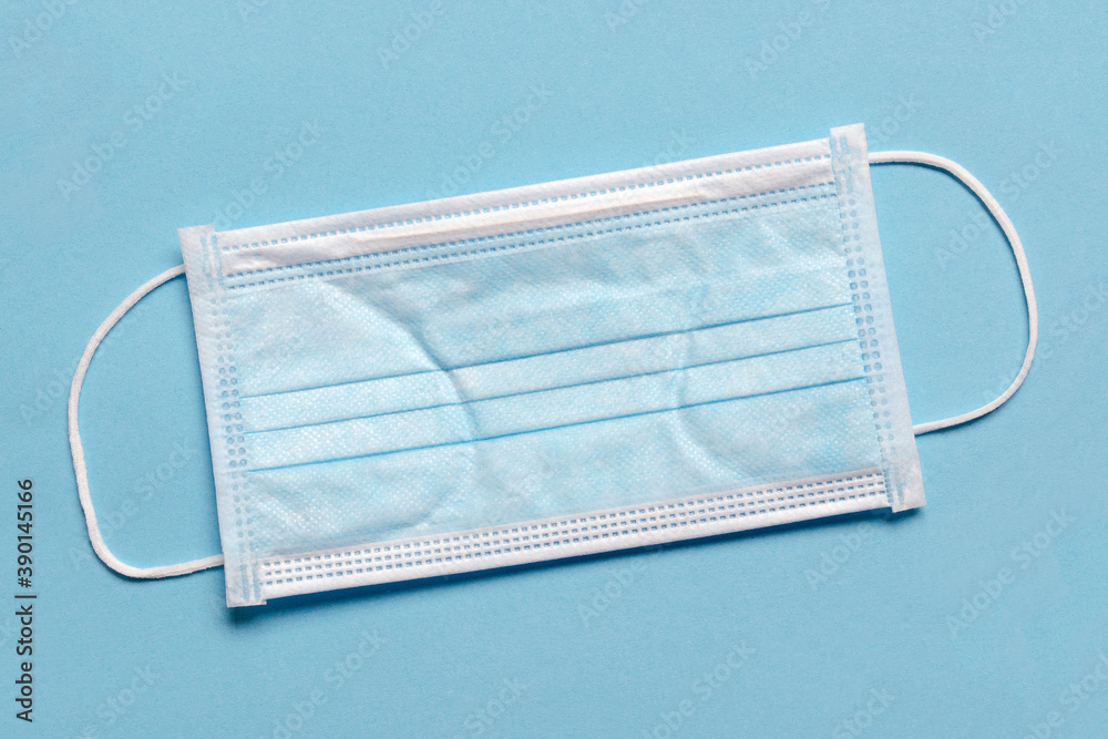 Medical mask on a blue background, top view. Surgical medical mask isolated on blue background. Prevent coronavirus. Medical 3-layer surgical mask covering nose and mouth. Disposable medical mask. Medical mask on a blue background, top view. Surgical medical mask isolated on blue background. Prevent coronavirus. Medical 3-layer surgical mask covering nose and mouth. Disposable medical mask.