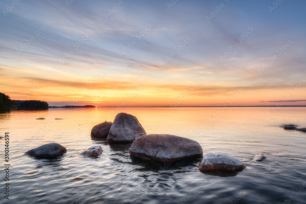 Summer sunset over Lake Onega in Karelia. Stones in the water against the background of the sunset sky.