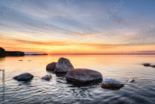 Summer sunset over Lake Onega in Karelia. Stones in the water against the background of the sunset sky.