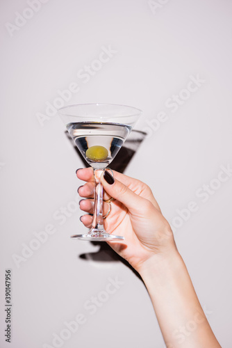 cropped view of woman holding glass of martini with olive on white