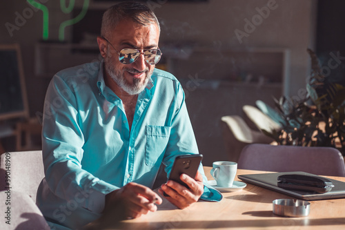 Man drinking morning coffee and smoking while looking at his phone.