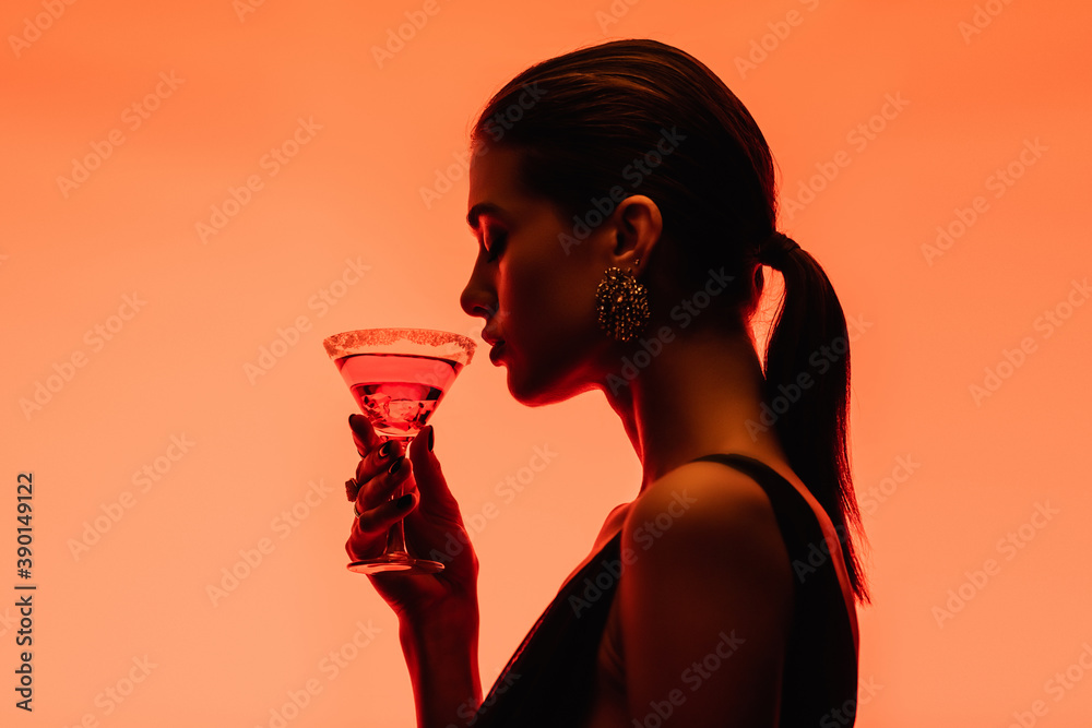 Side view of young woman holding margarita cocktail with ice cubes on orange - obrazy, fototapety, plakaty 