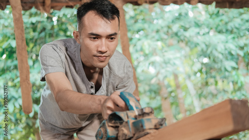close up of an asian carpenter working using an electric wooden dowel while grinding wood at a workshop