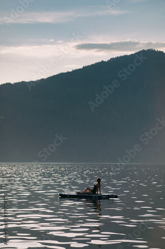 Girl at sunset on the lake on a stand-up paddle board in Altai