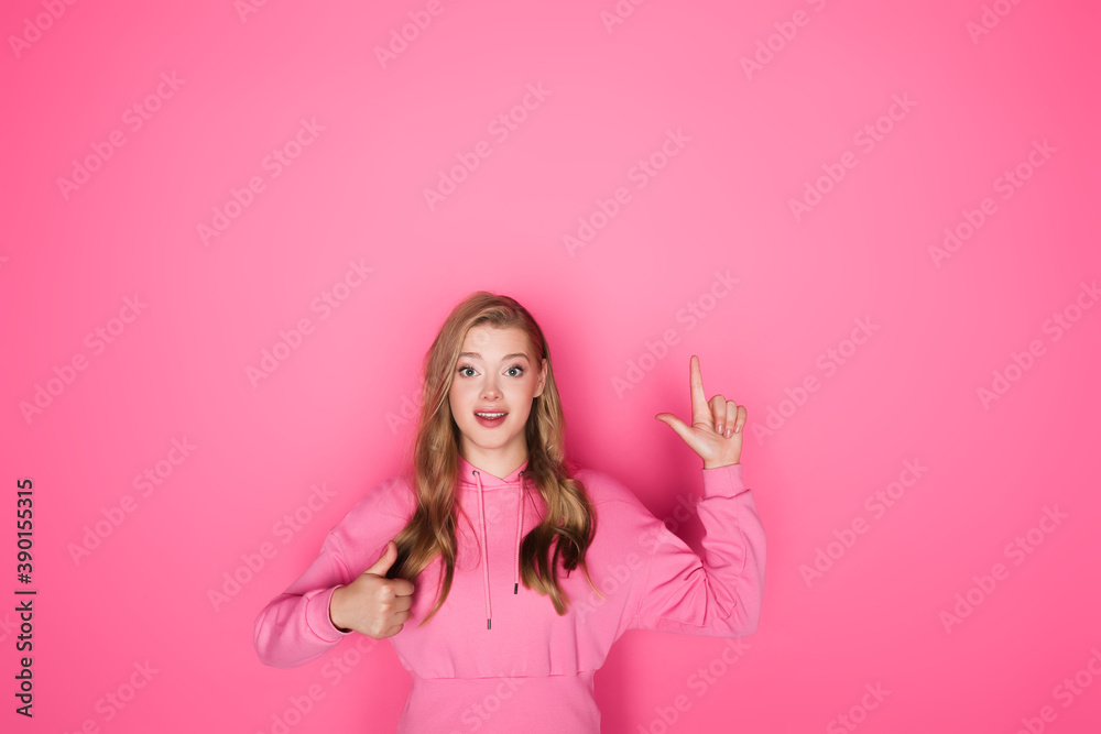smiling beautiful woman pointing with finger and showing thumb up on pink background smiling beautiful woman pointing with finger and showing thumb up on pink background