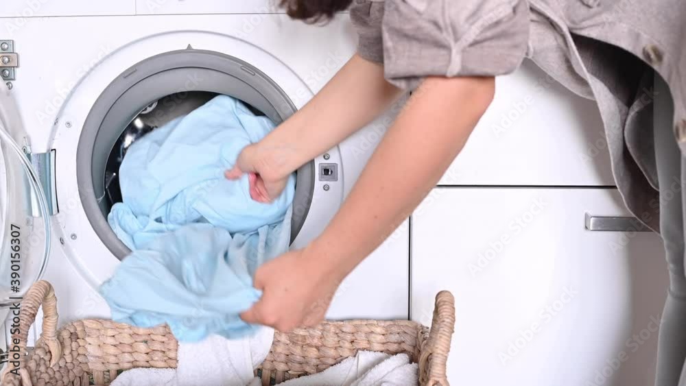 The woman puts the laundry into the washing machine from the basket. Hands and drum of a washing machine close-up. High quality 4k footage The woman puts the laundry into the washing machine from the basket. Hands and drum of a washing machine close-up. High quality 4k footage