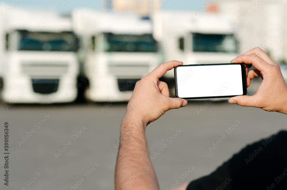 Mock up of a smartphone in the hands of a man. Against the backdrop of trucks. Logistics concept.