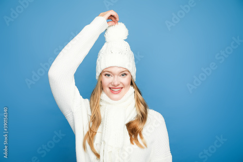 Schilderij op canvas happy blonde beautiful woman in winter white outfit touching pom pom on blue bac