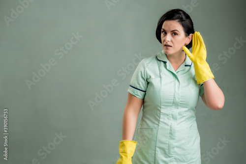Young cleaning woman wearing a green shirt and yellow gloves making can't hear you gesture © Cipri Suciu 