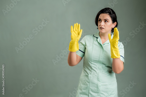 Young cleaning woman wearing a green shirt and yellow gloves showing fear, with her arms up © Cipri Suciu 