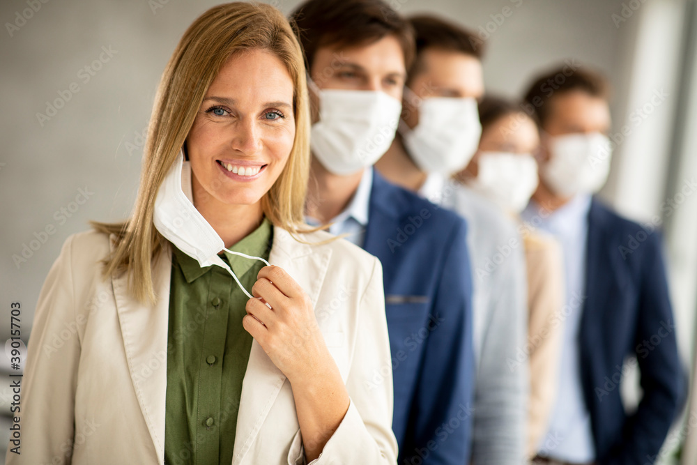 Business woman taking off her protective facial mask and looking at the camera with her team members standing in the line Business woman taking off her protective facial mask and looking at the camera with her team members standing in the line