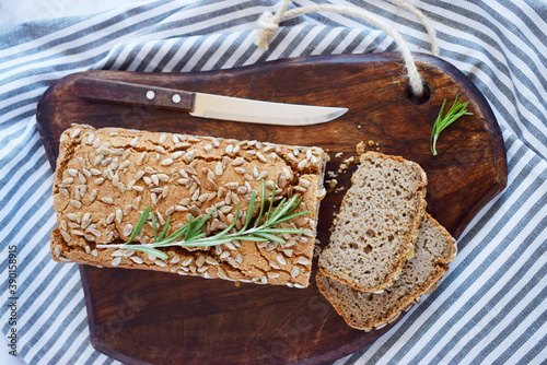 Glutenfree buckwheat bread with a golden brown crust, sprinkled with sunflower seeds, lies on a wooden table. Healthy homemade recipe. Grains of green buckwheat are scattered nearby. Top view