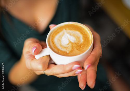 The cup of coffee in women hands .Lady's hands holding cup with sth heart-shaped. High quality photo