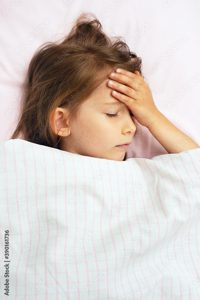 The sick child in bed put her hand on her forehead. Little girl with high fever and headache. The sick child in bed put her hand on her forehead. Little girl with high fever and headache.