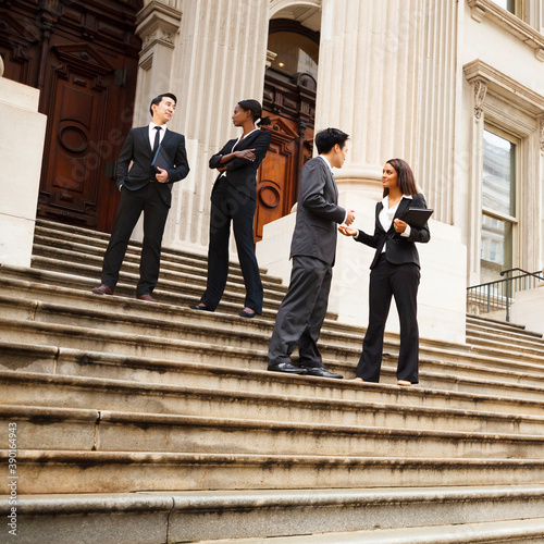Four well dressed professionals in discussion on the exterior steps of a building. Could be lawyers, government workers, business people etc.