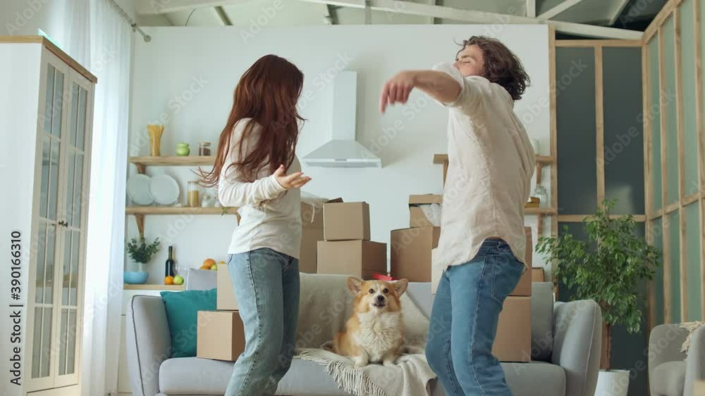 A Happy Couple Celebrating, Dancing, and Having Fun in Living Room With Boxes. YLovely Couple Having a Fun Together While Dancing. On the Couch Sitting a Funny Dog A Happy Couple Celebrating, Dancing, and Having Fun in Living Room With Boxes. YLovely Couple Having a Fun Together While Dancing. On the Couch Sitting a Funny Dog