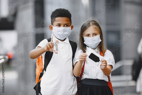 Mixed-races boy and little girl. Junior students in a medical masks. African American cute boy in white t-shirt. Coronavirus concept.