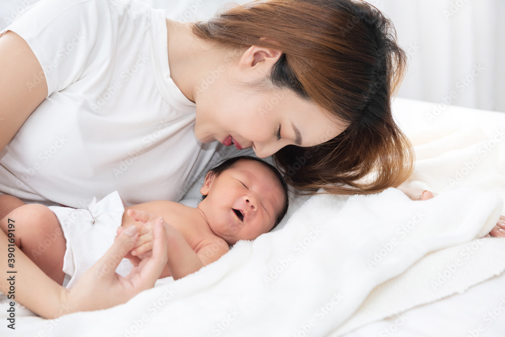 Beautiful asian women mother long hair in the white pajamas. mom kiss at newborn infant with love, while a baby sleeping in her arm with warm, safe, comforted resting on the clean bed. Beautiful asian women mother long hair in the white pajamas. mom kiss at newborn infant with love, while a baby sleeping in her arm with warm, safe, comforted resting on the clean bed.