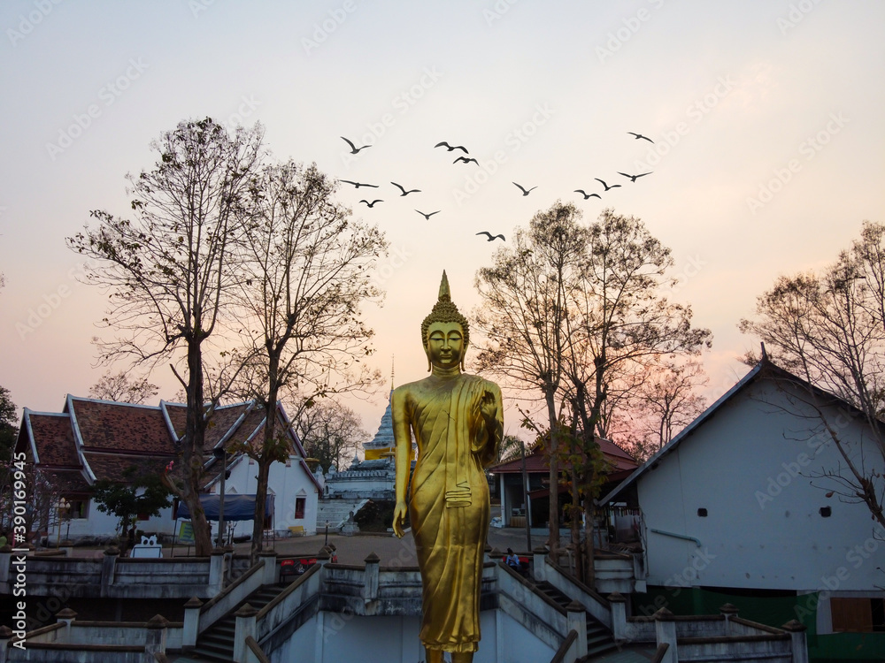 Fototapeta premium Nan / Thailand -February 2020 : Wat Phra That Khao Noi temple in Northern Thailand with a large golden standing Buddha statue over looking the city from the mountain top in sunset